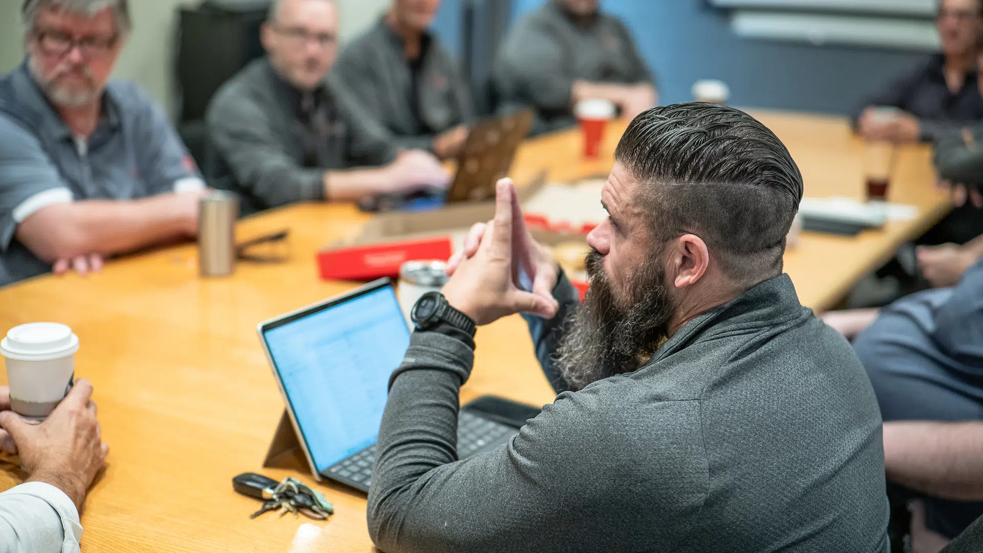A boardmeeting of Telexperts employees discussing business communications and VoIP systems. Eight are seated around a conference table, with one man in focus in the foreground.
